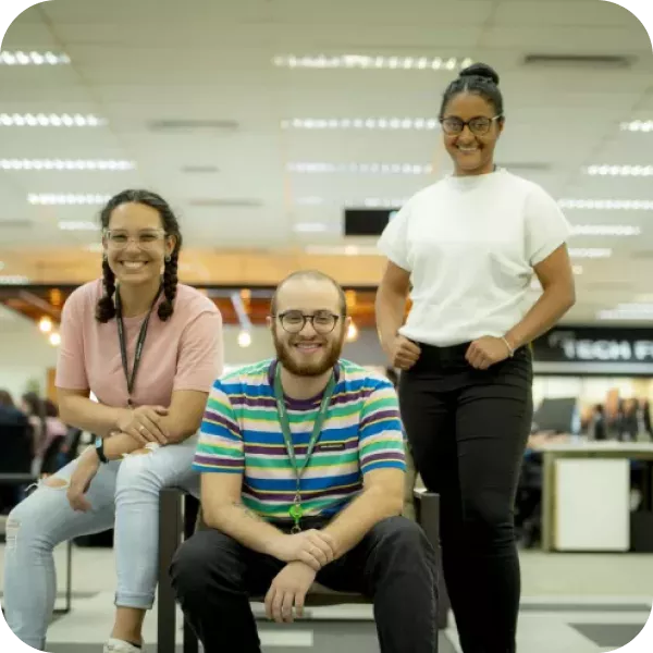 A wall display in a public service area with digital service sections. It features a large image of a smiling woman with glasses in the center, surrounded by digital screens and icons representing different electronic services. There are two orange kiosks with touch screens for self-service on the right side.